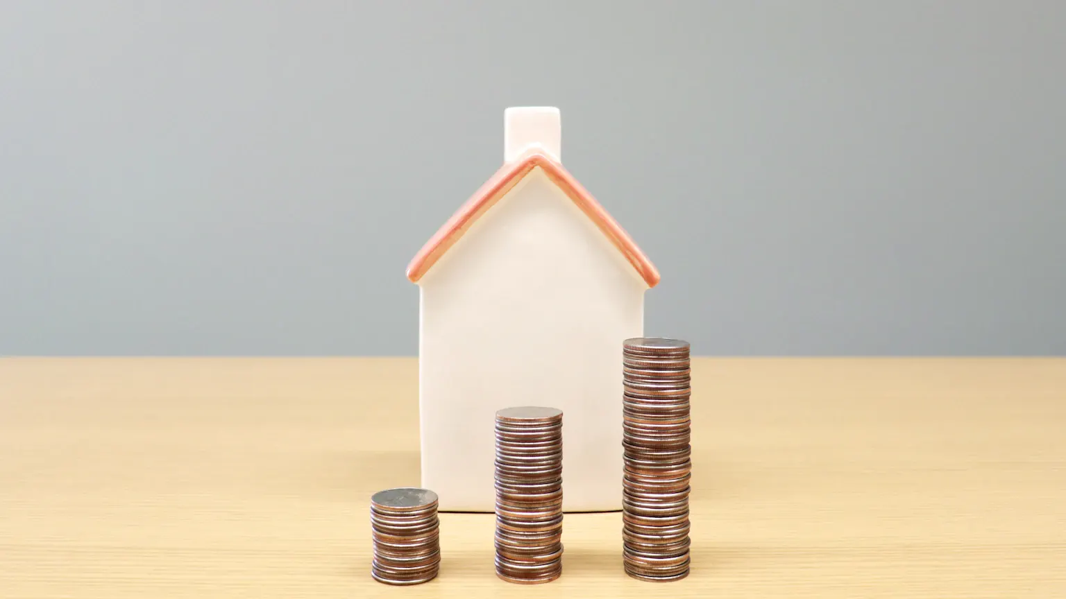 Maqueta de una casa junto a columnas de monedas